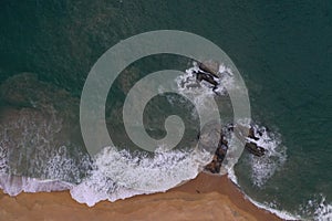 Aerial drone bird view shot of the sea shore with turquoise blue water, large white waves and foam, empty beach with yellow sand,
