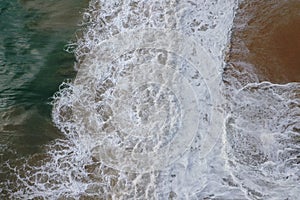 Aerial drone bird view shot of the sea shore with turquoise blue water, large white waves and foam, empty beach with yellow sand,