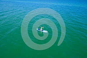 Aerial drone birds eye view of young woman exercising sup board in turquoise tropical clear waters