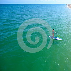 Aerial drone birds eye view of young woman exercising sup board in turquoise tropical clear waters