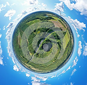 Aerial drone 360 degree view on wind turbine, snake shape road, wheat fields and forest during summer