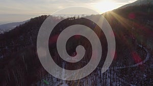 Aerial drone flight over snowy forest woods at sunset with people walking. Winter snow in mountain nature outdoors