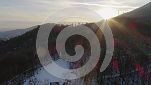 Aerial drone flight over snowy forest woods at sunset with people walking. Winter snow in mountain nature outdoors