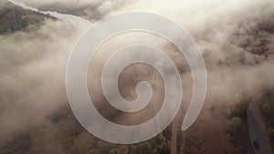 Aerial drone flight view over low clouds and morning mist covered mountain slopes at sunrise. Sunrise in mountains