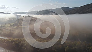 Aerial drone flight view over low clouds and morning mist covered mountain slopes at sunrise. Sunrise in mountains