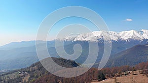 Aerial: drone flying over forest in springtime, aerial view of snow capped mountain range and valley on the Alps, clear blue sky,
