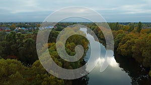 Aerial drone flying over a rural river with trees on the bank before the start of a thunderstorm.