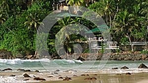 Aerial drone footage captures luxury villa nestling among lush palm trees by gentle waves on golden sand Mirissa beach