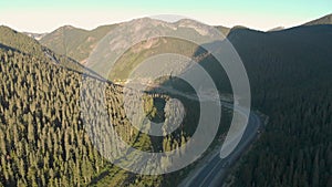 Aerial drone footage of rugged mountain peak next to Trans Canada highway at sunrise with a semi truck transporting