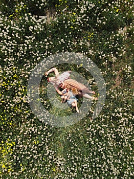 Aerial drone: Mother having quality funny playing time with her baby girls at a park blowing dandelion - Young blonde