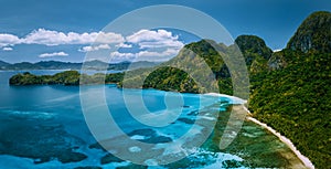 Aerial drone panoramic view of uninhabited tropical island with rugged mountains, rainforest jungle and big blue bay