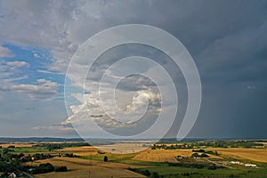 Aerial drone perspective view on dark storm clouds over the green scenery with green forests, yellow wheat fields, green meadows