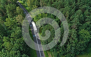 Aerial drone perspective view on white truck with cargo trailer riding through the forest on curved asphalt road