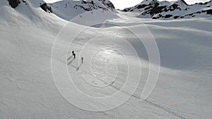 Aerial / drone shot of apline mountains & skiers walking up the mountain with ski`s and poles for support