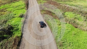 Aerial drone shot of a black passenger car traveling down a remote gravel road.