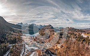 Aerial drone shot of Hohenschwangau by lake in Fussen with view of Alps snow mountain range in Germany winter