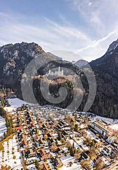 Aerial drone shot of picturesque Neuschwanstein Castle with view of snowy village in German Fussen winter sunlight