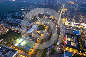 aerial drone shot showing brightly lit street with multi story sky scrapers offices, homes, shopping malls, sports