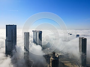Aerial Drone shot of skyscrapers in the city with fog clouds passing by - Abu Dhabi Al Reem island, Sun, Sky and Gate towers
