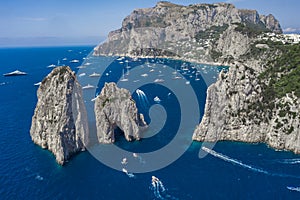 Aerial drone shot view of faraglioni limestone crags in summer in Tyrrhenian sea with yachts off Capri Island