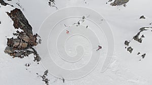 AERIAL DRONE Skier and snowboarder going off piste on extreme slope in snowy mountains, jumping, freeride