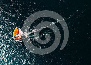 Aerial drone top down photo of a sailboat with a bright orange mast against a deep blue ocean