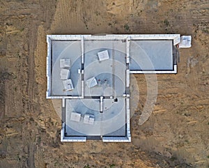 Aerial drone top down view on construction site with reinforced concrete house foundation, poured concrete floor and brick walls