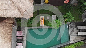 Aerial Drone top down view of slim young woman in beige bikini relaxing and get sunbathe near swimming pool in chaise