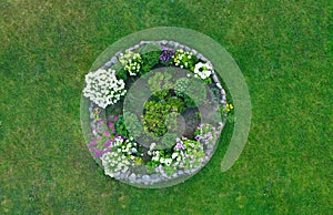 Aerial drone top down view on stylish round flowerbed surrounded by rock wall with violet, white and yellow blooming flowers.