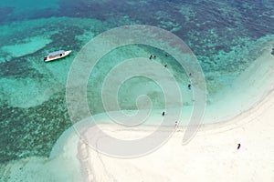 Aerial drone top view of people snorkeling over coral reef with clear blue ocean water with boat and walk on white sand beach.