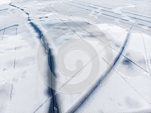 Aerial drone top view of snow covered frozen lake or river surface with big cracked ice diagonal lines. Natural winter
