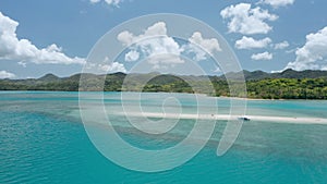 Aerial drone - tourist banca boat moored at sandbar from the distance. Main land and white clouds moves in background