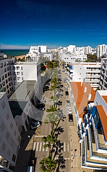 Aerial drone vertical view of street lined with palm trees in tourist Portuguese city of Quarteira, Algarve, Portugal
