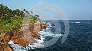 Aerial drone video of dynamic ocean waves hitting tropical coast with rocks and palm trees. Inviting blue water, plants