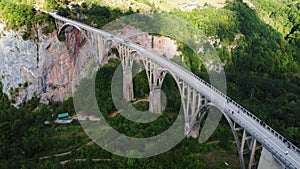 Aerial drone view of arched Djurdjevica Bridge with moving cars over Tara river canyon in Montenegro, green landscape in