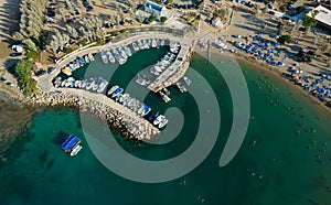 Aerial drone view of beach with people swimming and fishing boats moored at the harbor. Protaras Paralimni Cyprus