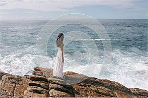 Aerial drone view of bride in an amazing dress standing on a cliff and looking at the sea