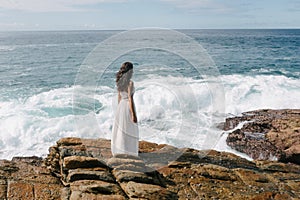 Aerial Drone View of a Bride, Brunette Girl in White Wedding Dress on Cliff Against Sea Background