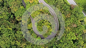 Aerial drone view of a car driving on a twisty road surrounded by a green forest