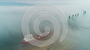 Aerial drone view of cargo ship and industrial cranes in fog in the sea harbor