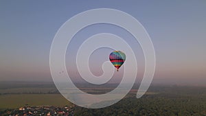 Aerial drone view of colorful air balloon flying over green park and river in small european city at summer sunrise