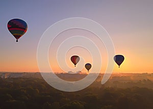 Aerial drone view of colorful hot air balloons flying over green park and river in small european city at summer sunrise