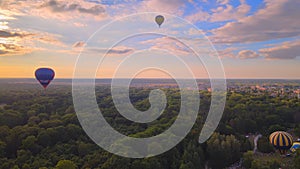 Aerial drone view of colorful hot air balloons flying over green park and river in small european city at summer sunrise