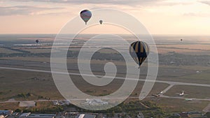 Aerial drone view of colorful hot air balloons flying over green park and river in small european city at summer sunset