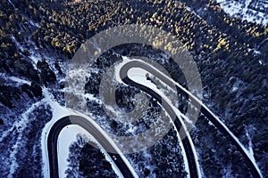 Aerial drone view of a curved winding road through the forest high up in the mountains in the winter with snow covered