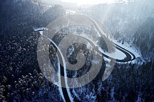 Aerial drone view of a curved winding road through the forest high up in the mountains in the winter with snow covered