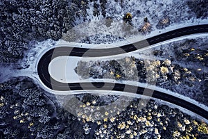 Aerial drone view of a curved winding road through the forest high up in the mountains in the winter with snow covered