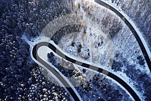 Aerial drone view of a curved winding road through the forest high up in the mountains in the winter with snow covered