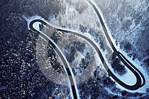 Aerial drone view of a curved winding road through the forest high up in the mountains in the winter with snow covered