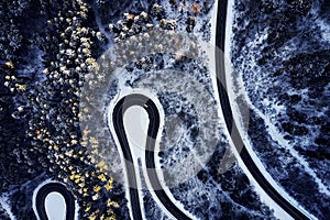 Aerial drone view of a curved winding road through the forest high up in the mountains in the winter with snow covered